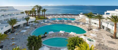 A resort with a large central pool, multiple smaller pools, and a view of the ocean.