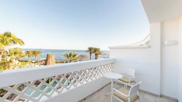 A balcony with a view of the sea, white furniture, and a pool area.