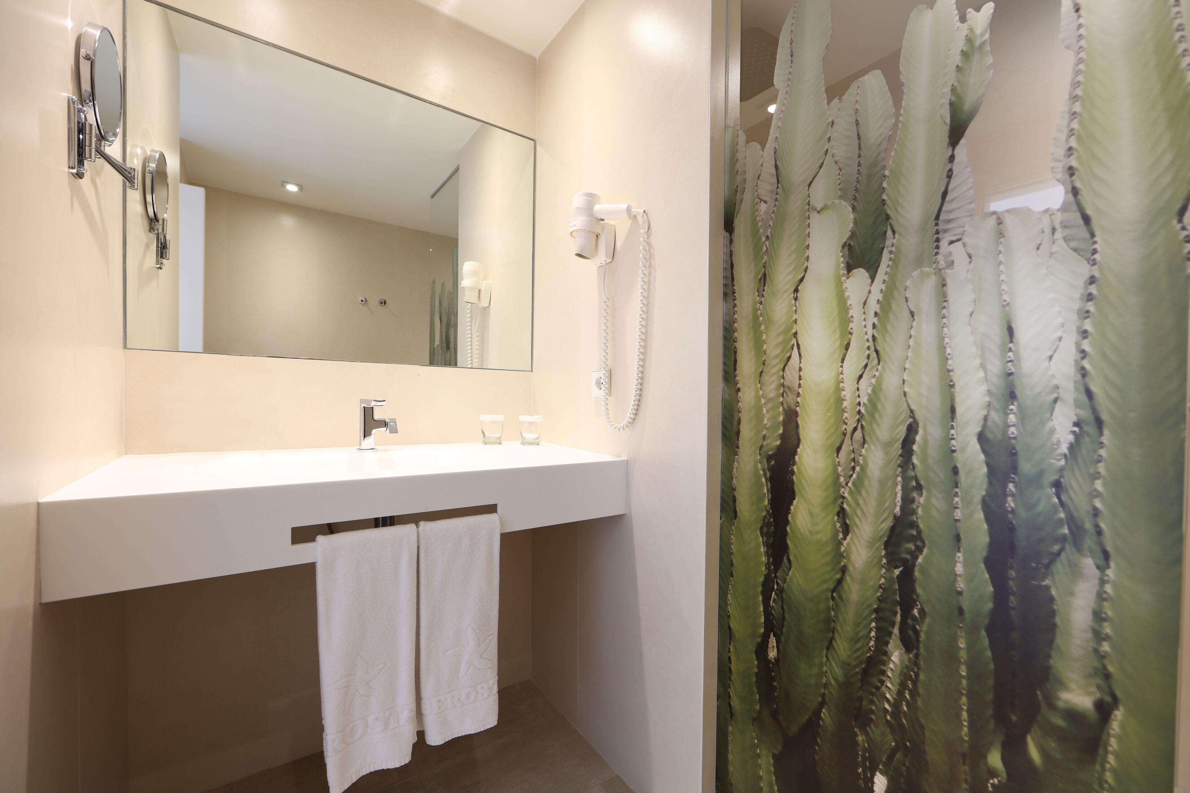 A bathroom with a white sink, a mirror, a hairdryer, and a shower curtain with a cactus pattern.