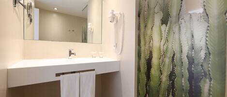 A bathroom with a white sink, a mirror, a hairdryer, and a shower curtain with a cactus pattern.