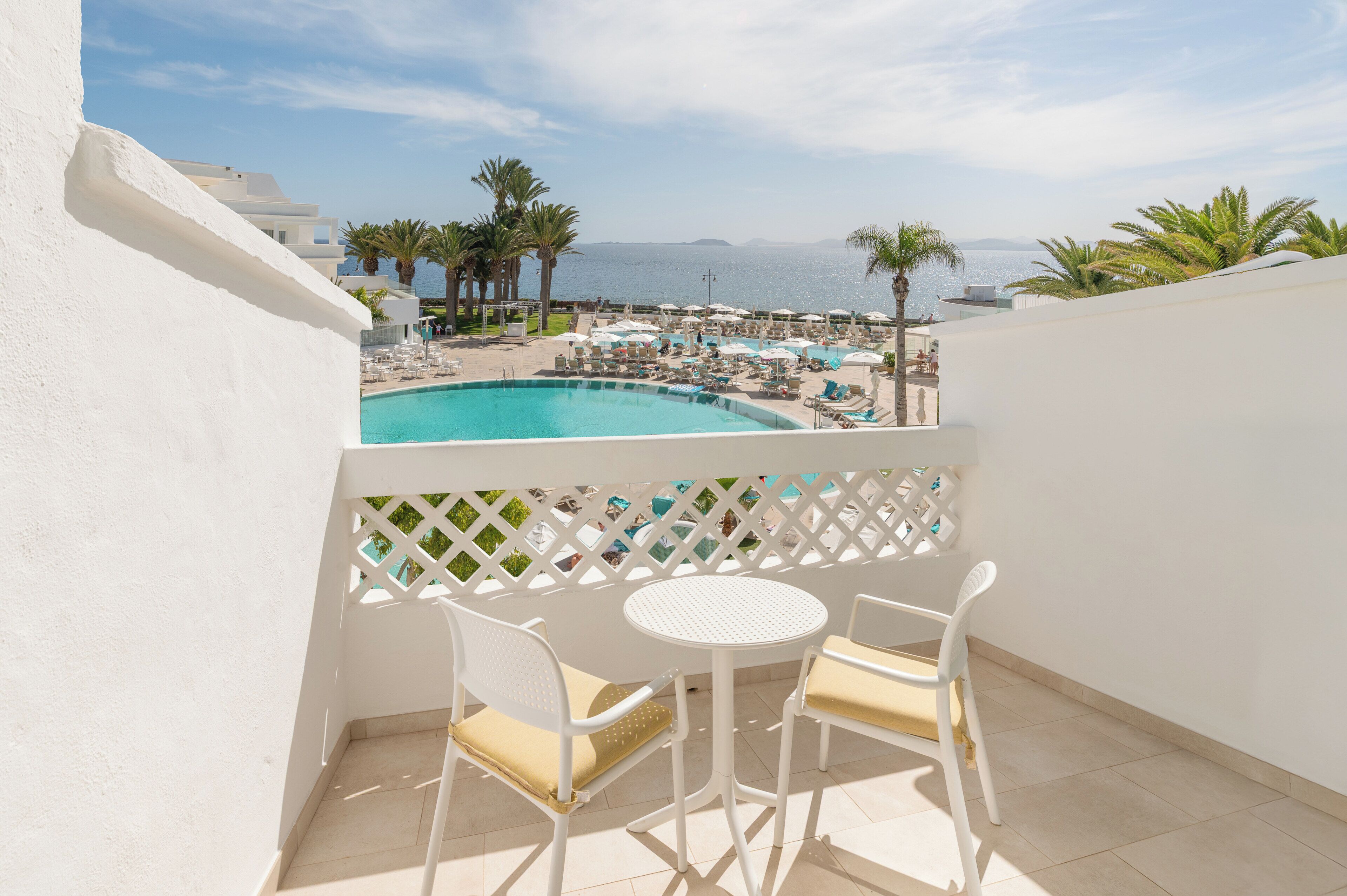 A balcony with a pool view, white chairs, and a white table.