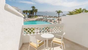 A balcony with a pool view, white chairs, and a white table.