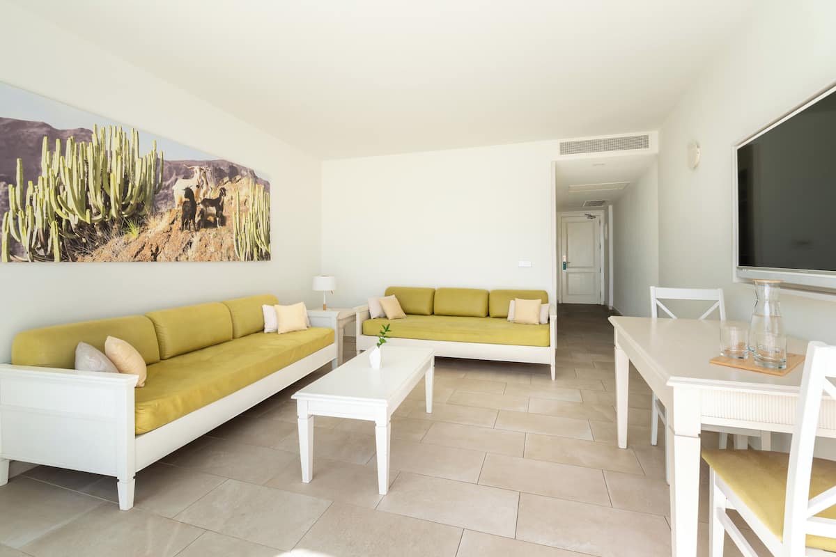 Una sala de estar con sofá amarillo, una mesa de centro blanca y un cuadro de cactus.