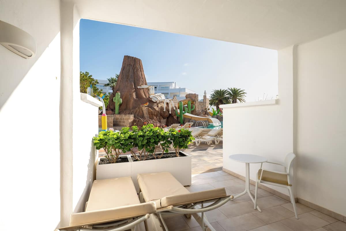 Un balcón con vistas a una piscina, sillones de descanso, una mesita y plantas en macetas.