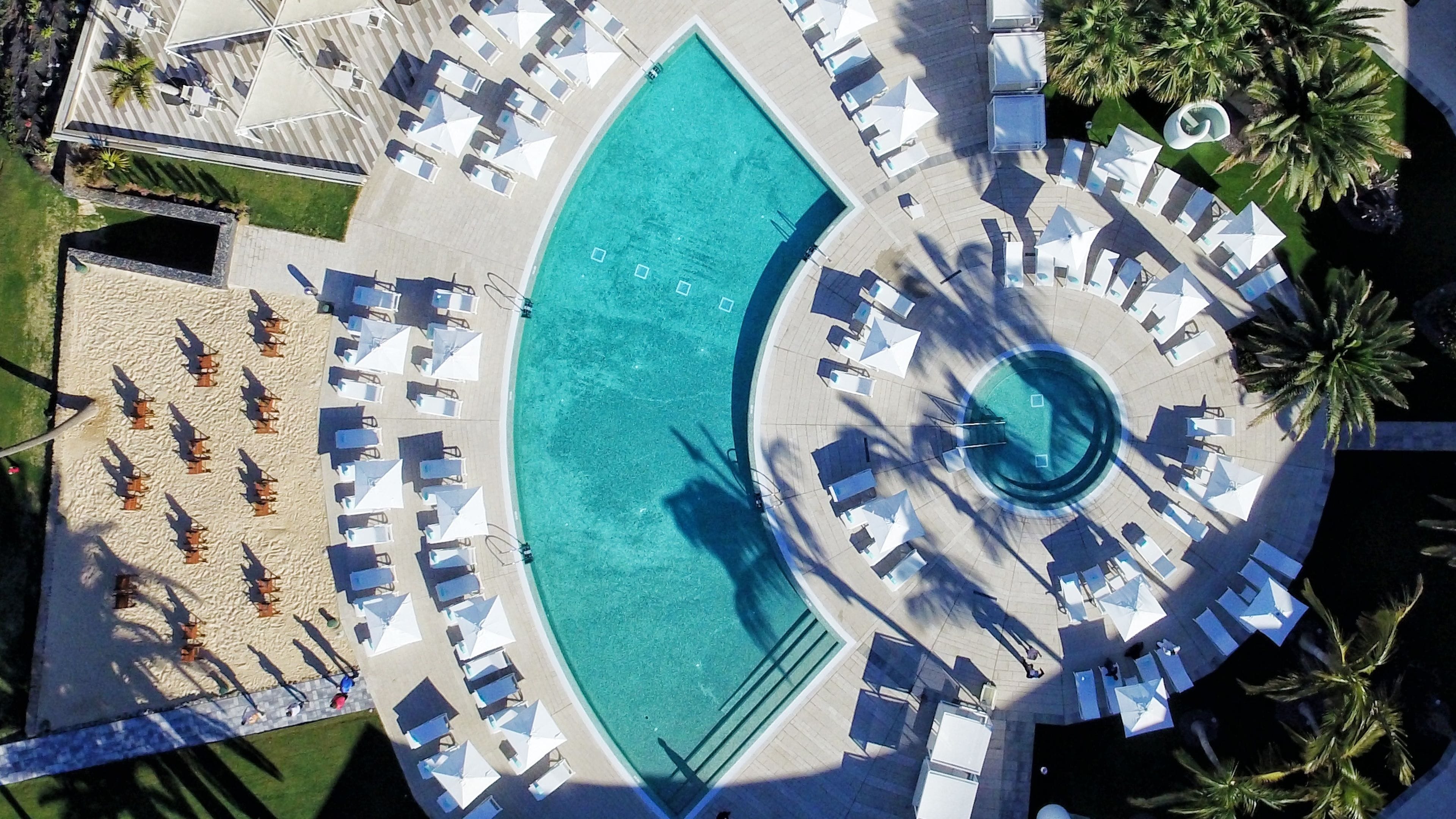 An aerial view of a resort with a large pool, sun loungers, and palm trees.