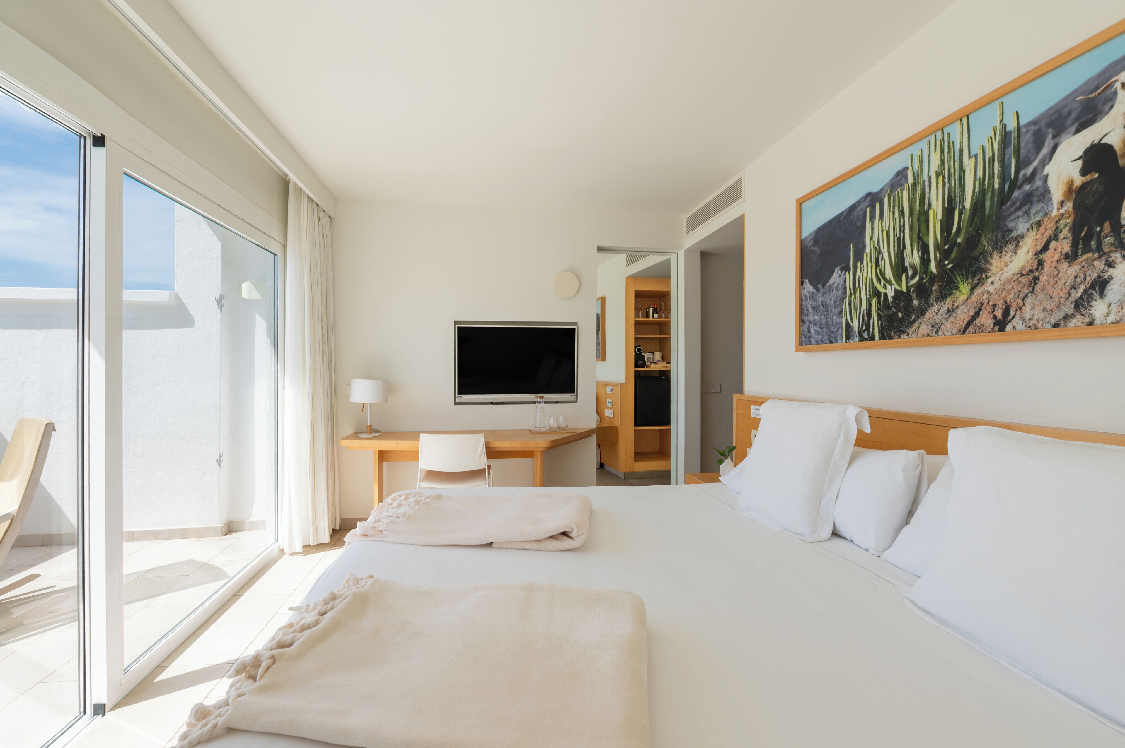 A hotel room with a bed, a desk, a TV, and a large window.
