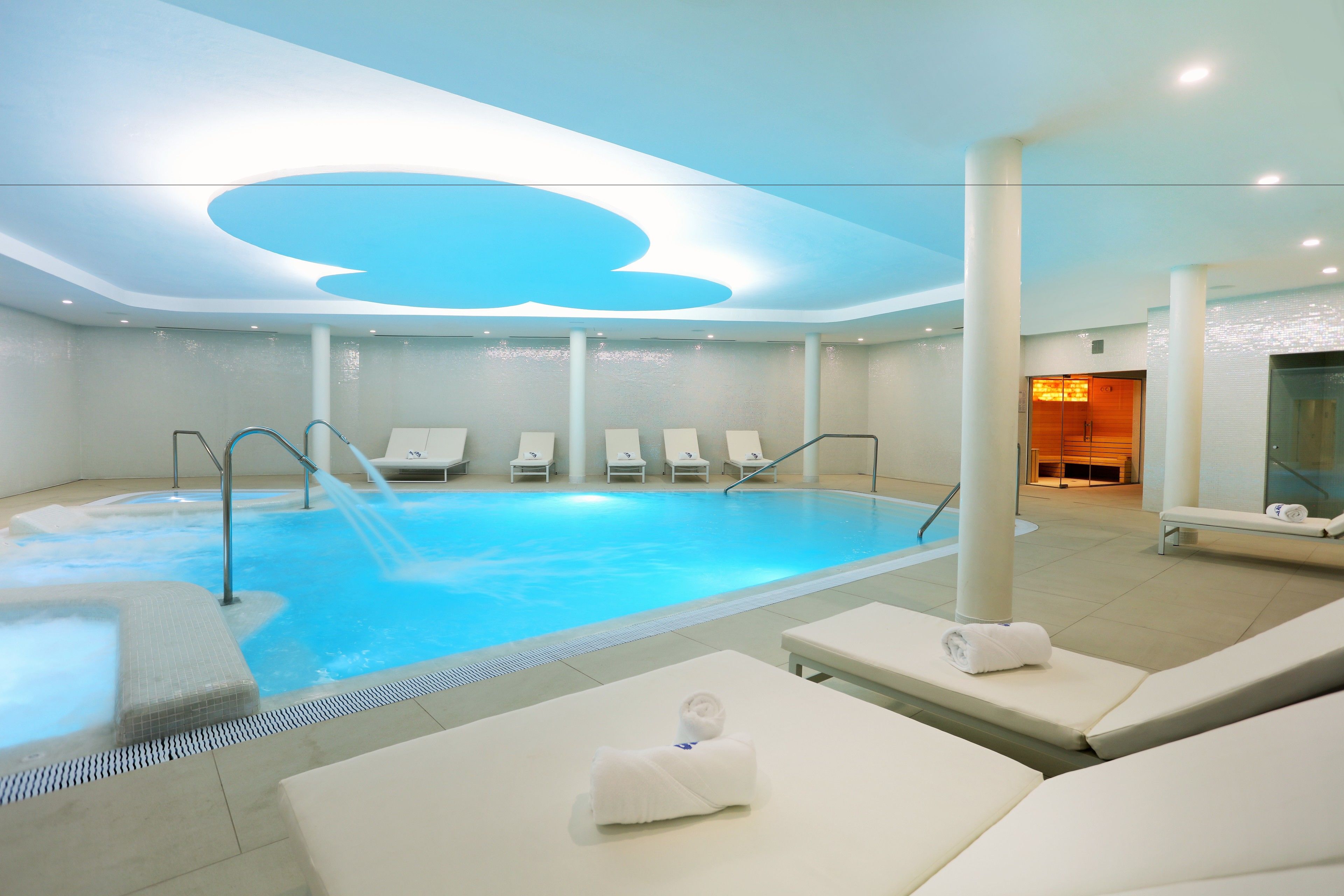 Un área interior de piscina moderna con sillones de descanso y una fuente.