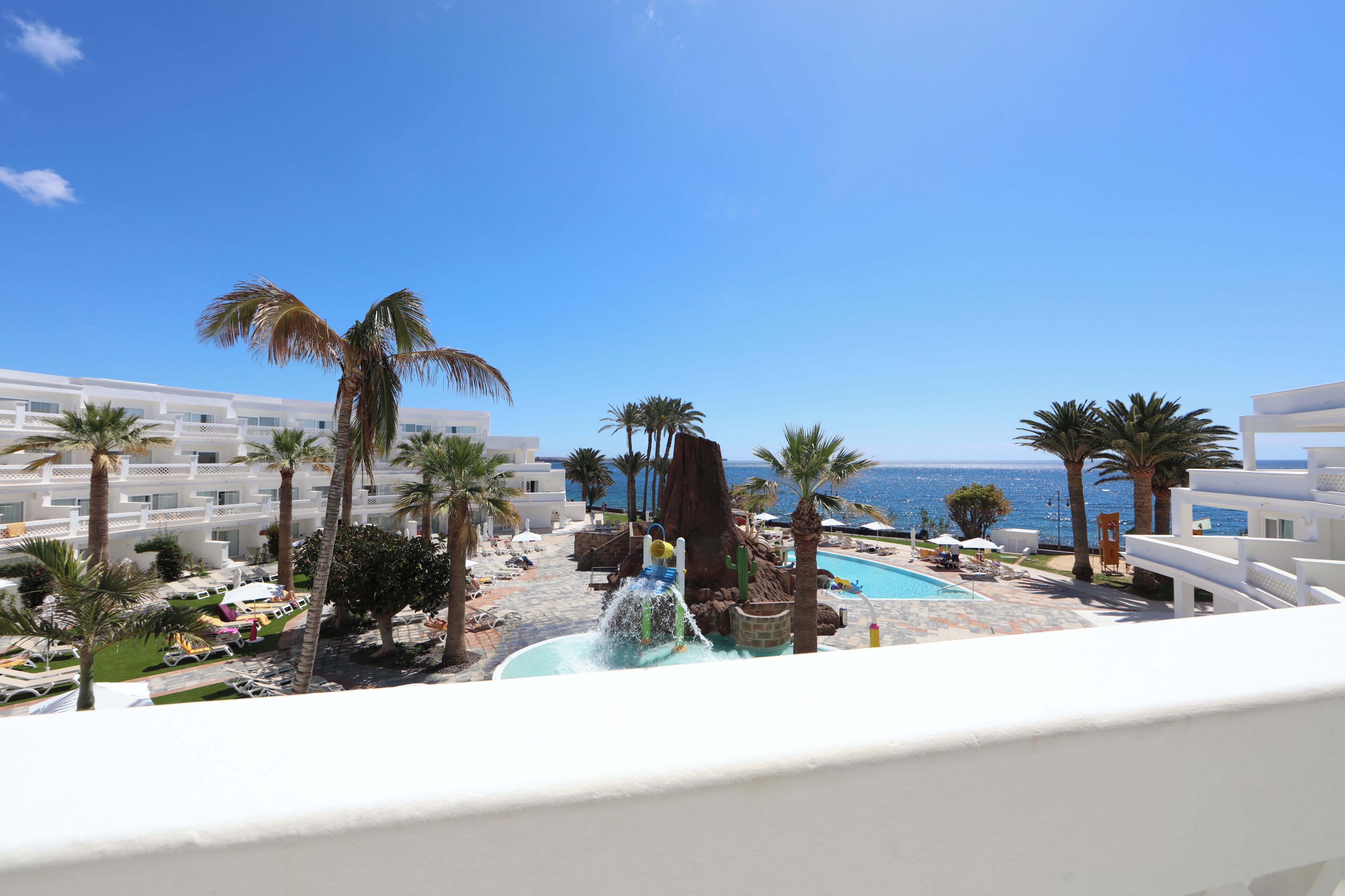 A resort with a pool, palm trees, and a view of the sea.
