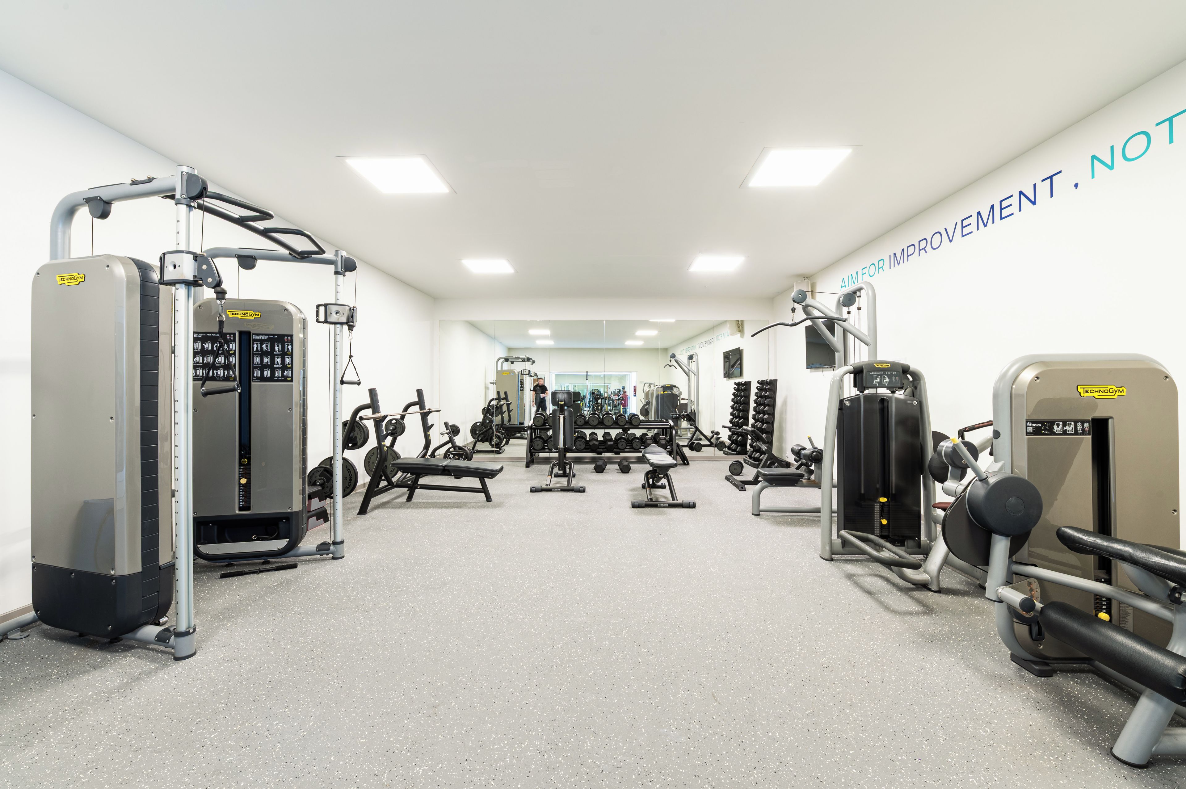 Un gimnasio con diferentes máquinas de ejercicio, pesas y un espejo grande.