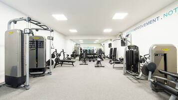 Un gimnasio con diferentes máquinas de ejercicio, pesas y un espejo grande.