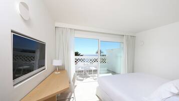 Habitación de hotel con cama, escritorio, silla, televisor y balcón con vista al mar.