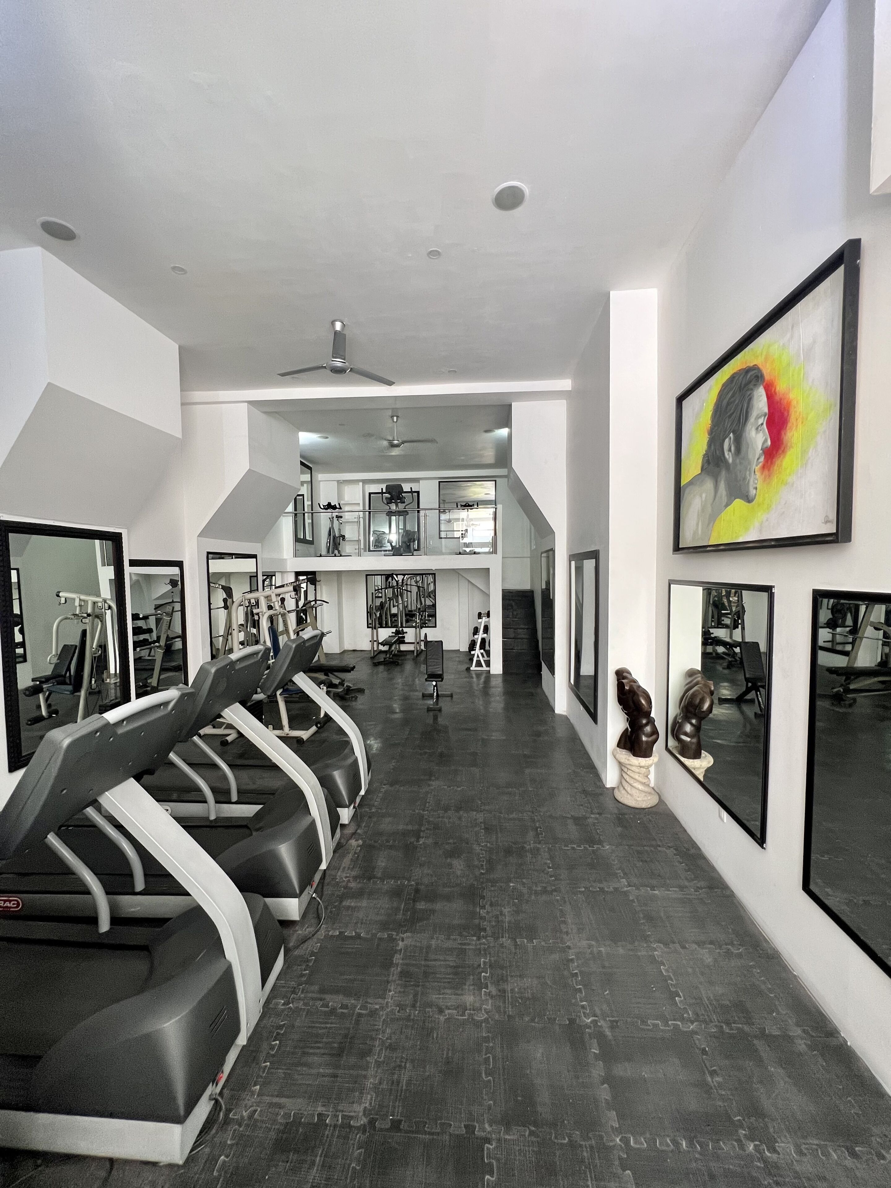Un gimnasio con cintas de correr, equipamiento de ejercicio y un espejo grande.