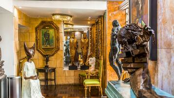 Una lussuosa hall con decorazioni elaborate, tra cui un grande specchio, statue dorate e una poltrona rivestita in verde.