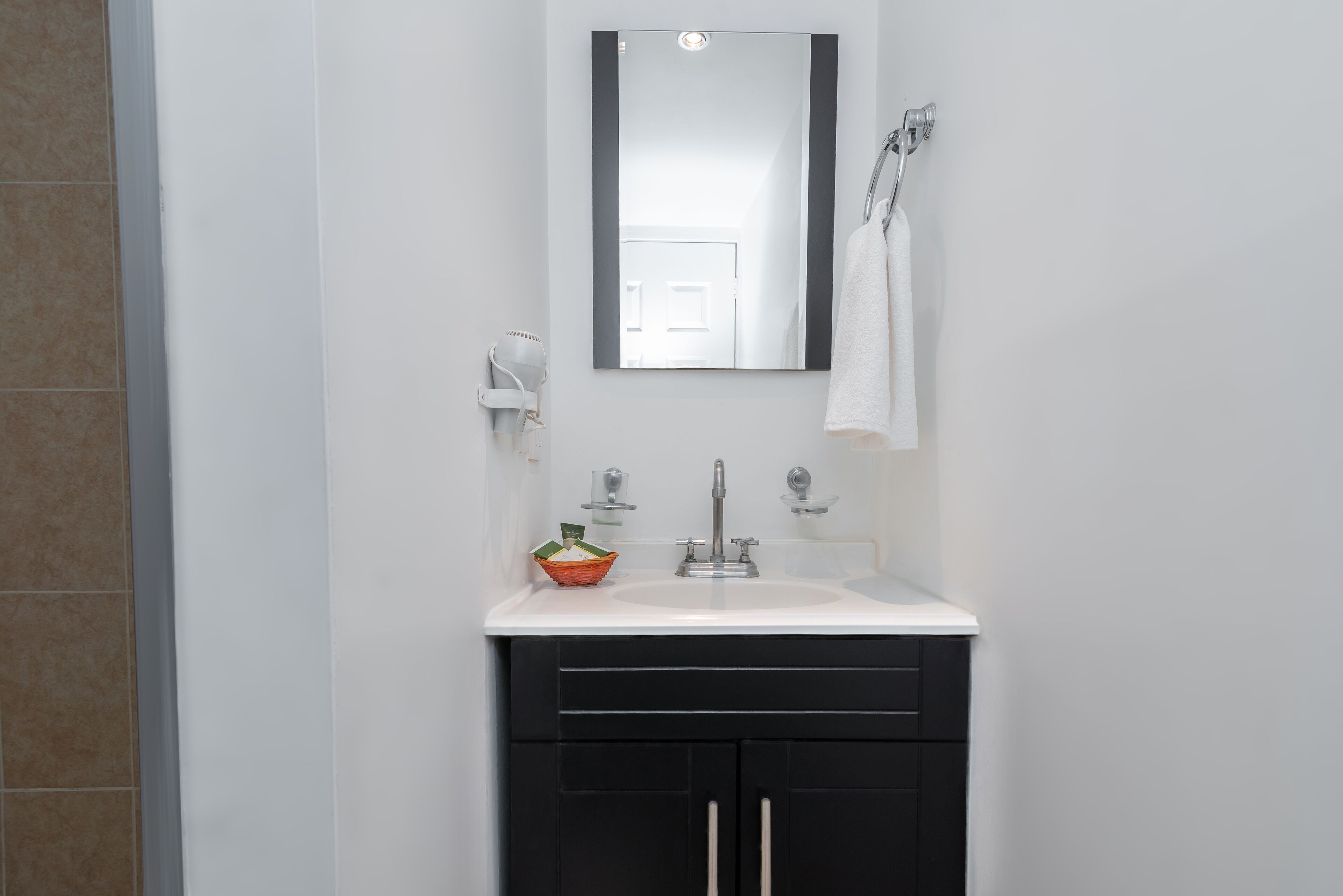 Een badkamer met een witte wastafel, zwarte kastjes, een spiegel en een handdoek aan een rek.