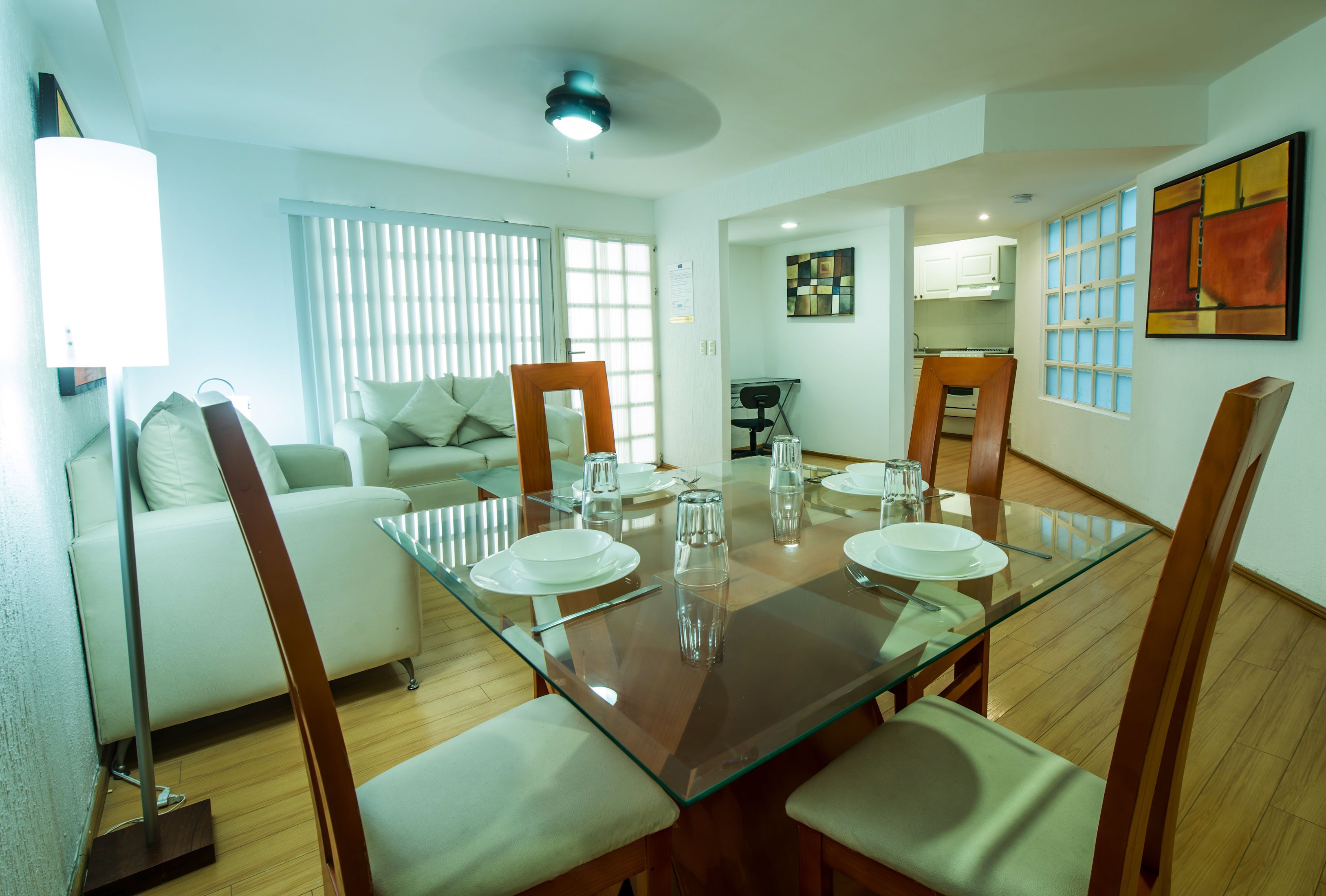 Un área de comedor con una mesa de vidrio, sillas de madera y un sofá blanco al fondo.