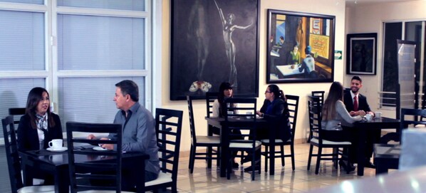 A restaurant with tables and chairs, paintings on the walls, and a window with blinds. - European Life Style Executive Suites & Gallery (Zapopan)