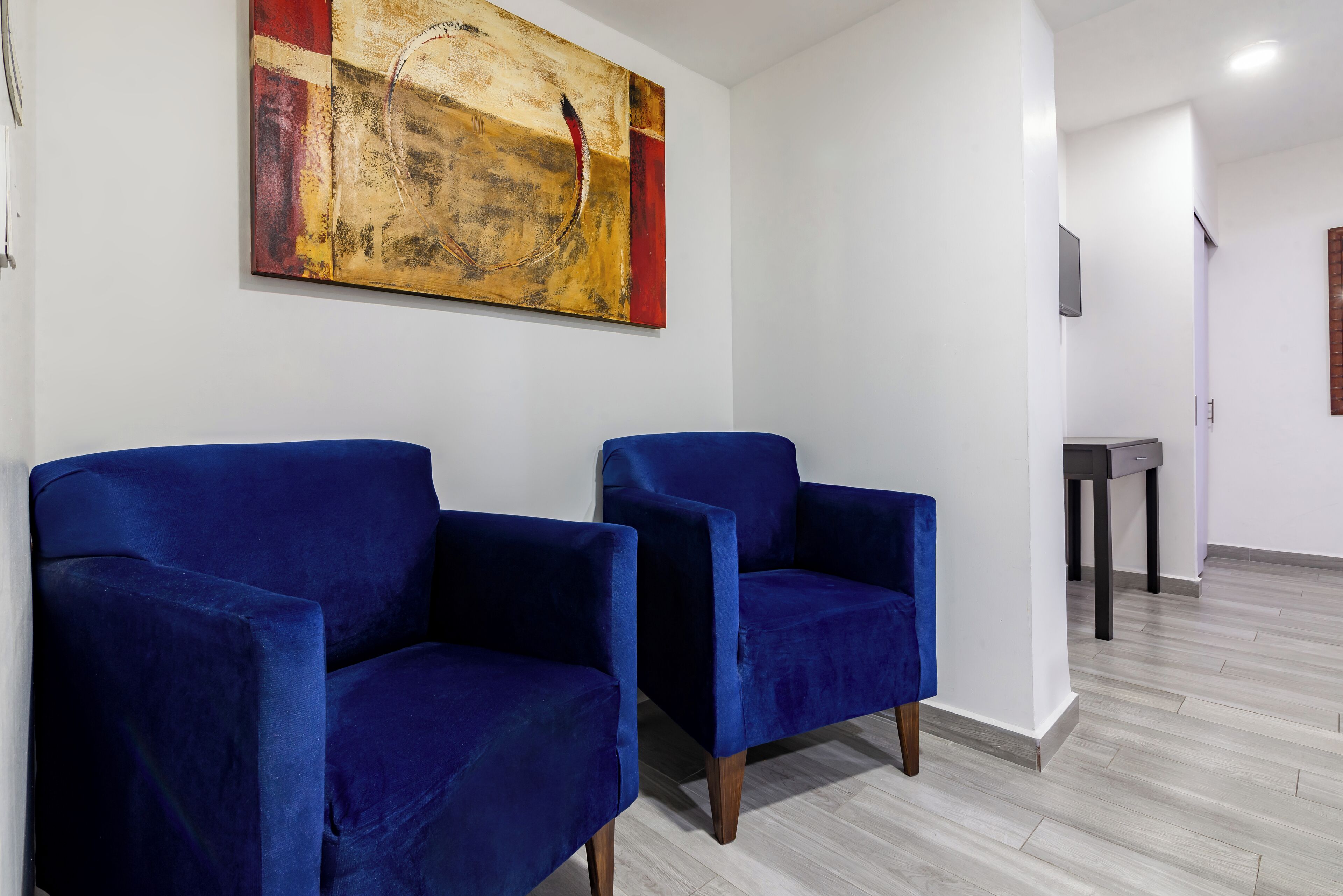 Una habitación con dos sillones azules, suelo de madera y un cuadro abstracto grande en la pared.