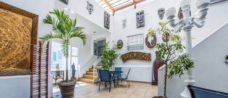 A spacious indoor area with a high ceiling, a staircase, and a dining area with chairs and a table.