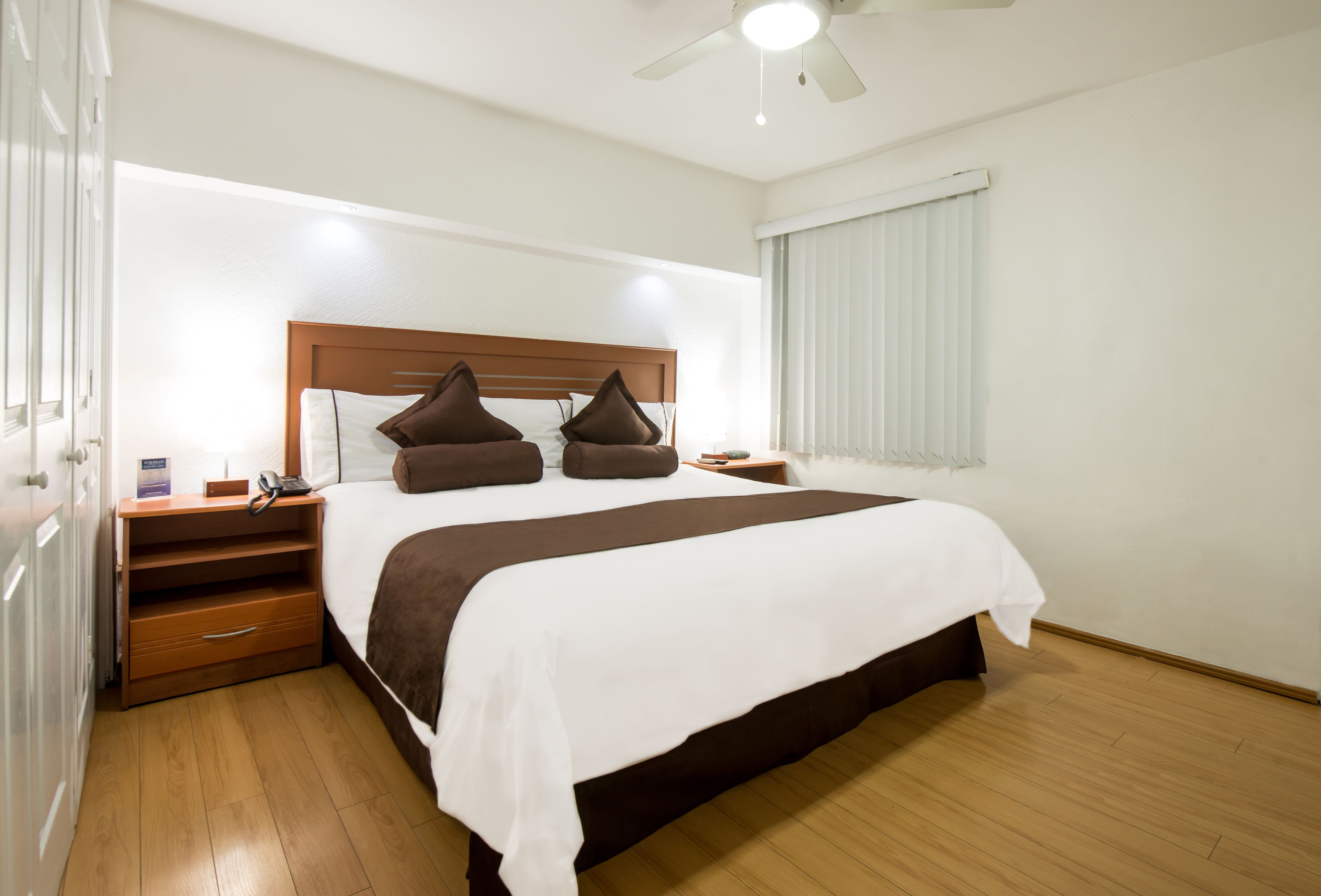 A hotel room with a large bed, wooden headboard, bedside tables, a telephone, and a ceiling fan.