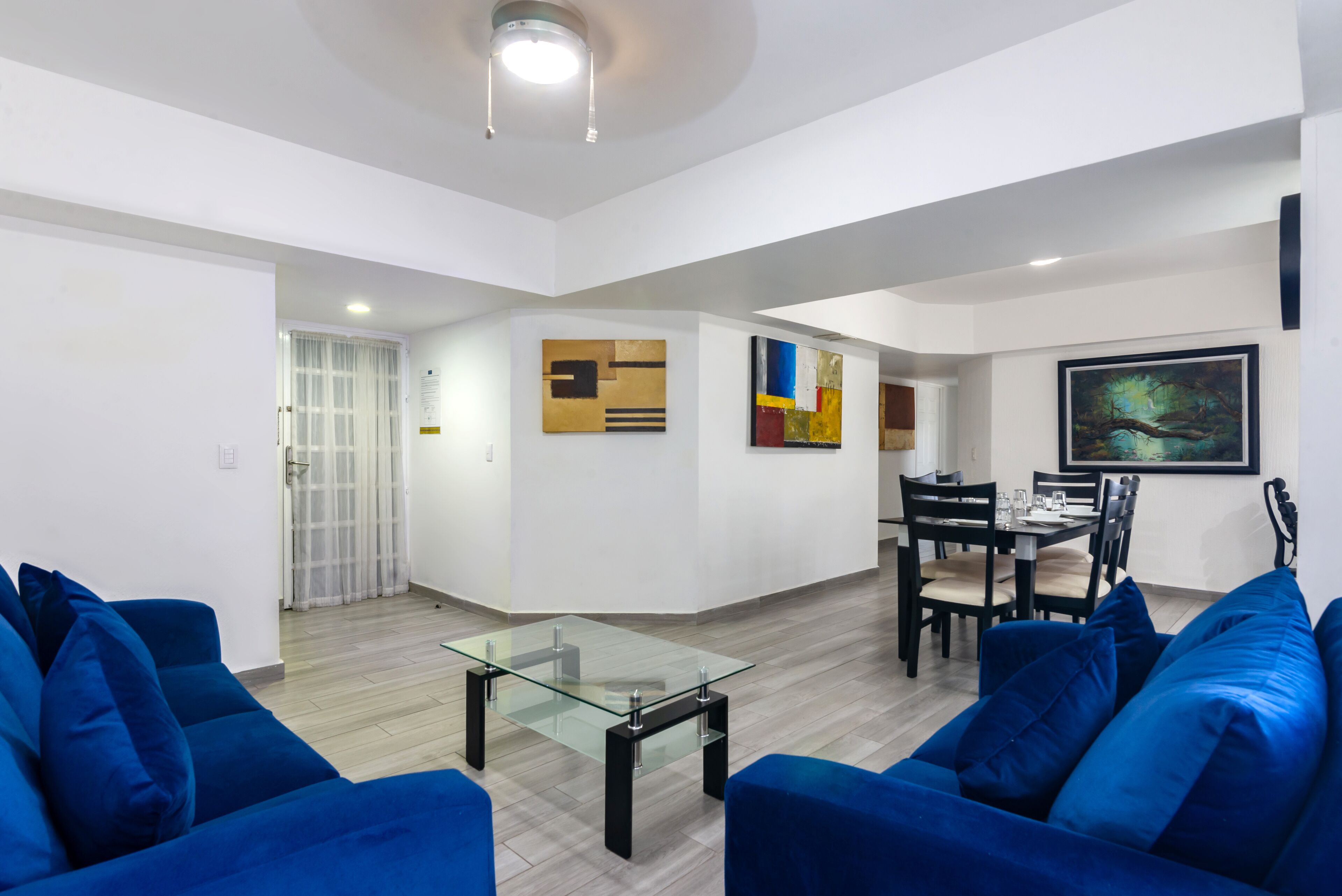 Uma sala moderna com uma mesa de centro de vidro, sofás azuis e uma área de jantar com cadeiras e mesa.