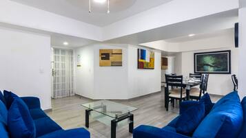 Uma sala moderna com uma mesa de centro de vidro, sofás azuis e uma área de jantar com cadeiras e mesa.