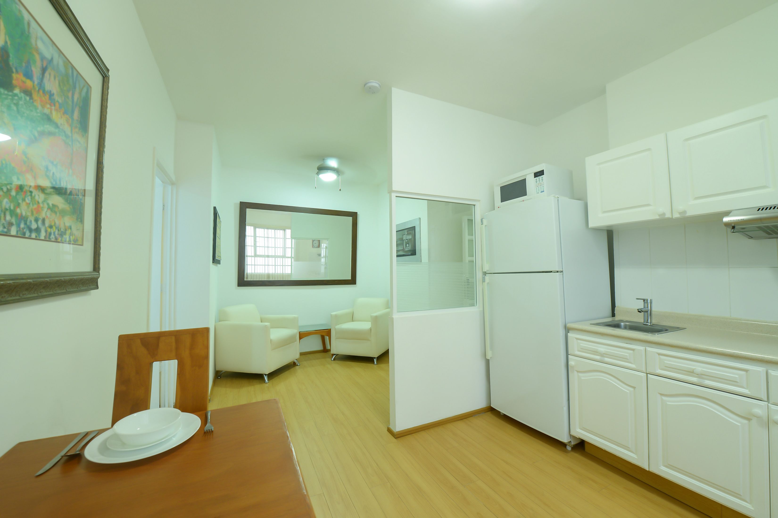 A modern kitchen with white cabinets, a refrigerator, and a dining area with a wooden table and chairs.