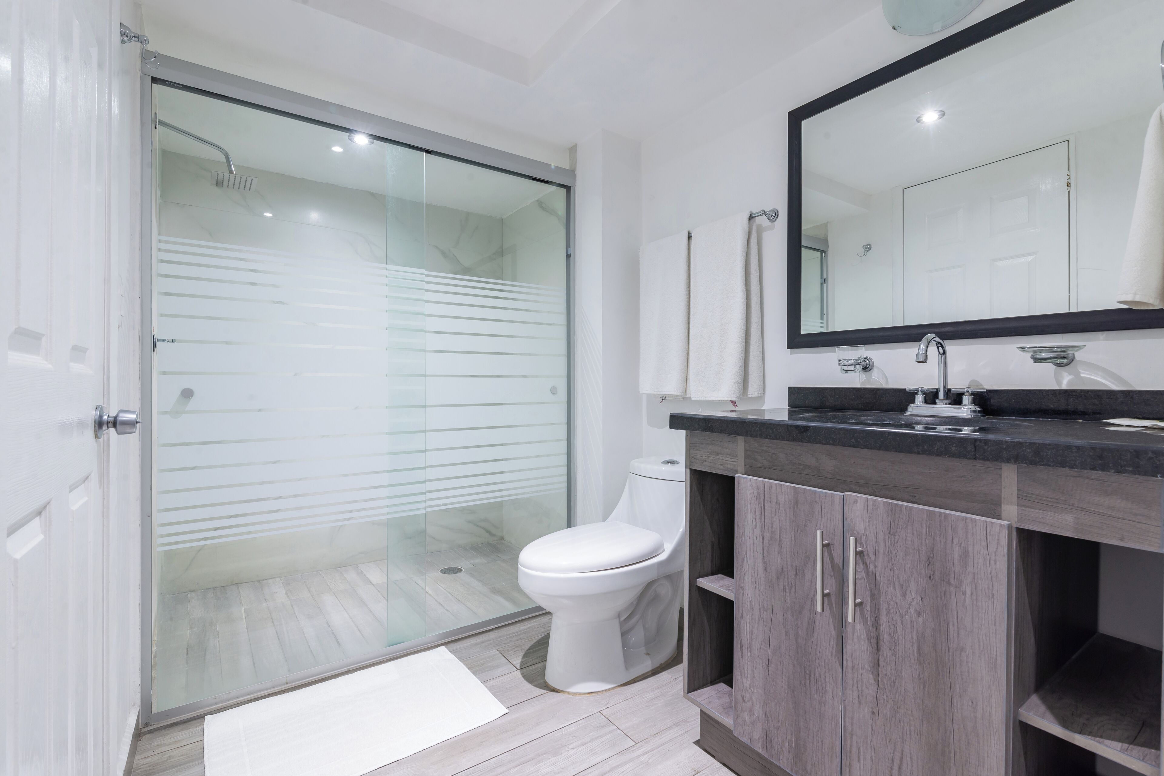Un baño moderno con cabina de ducha de vidrio, inodoro blanco y tocador de madera oscura con un espejo grande.