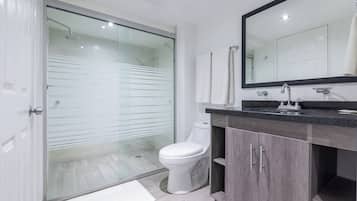 Un baño moderno con cabina de ducha de vidrio, inodoro blanco y tocador de madera oscura con un espejo grande.