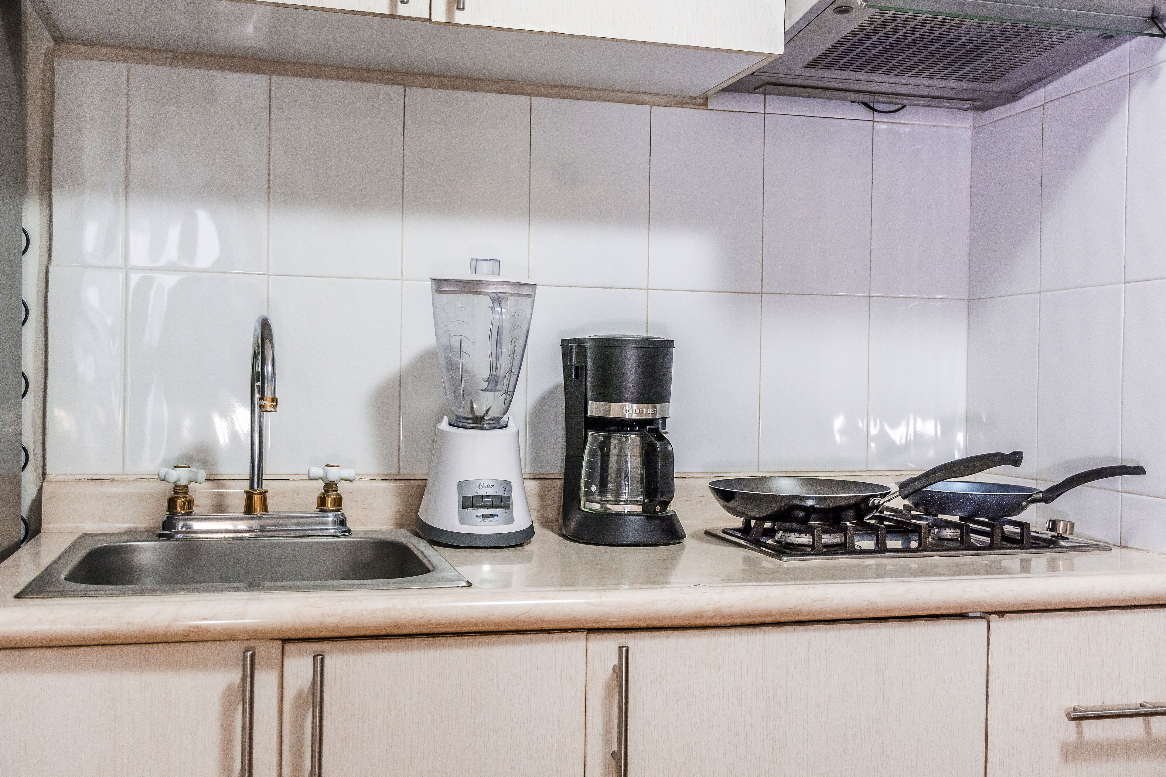 A kitchen with a sink, a blender, a coffee maker, and a stove.