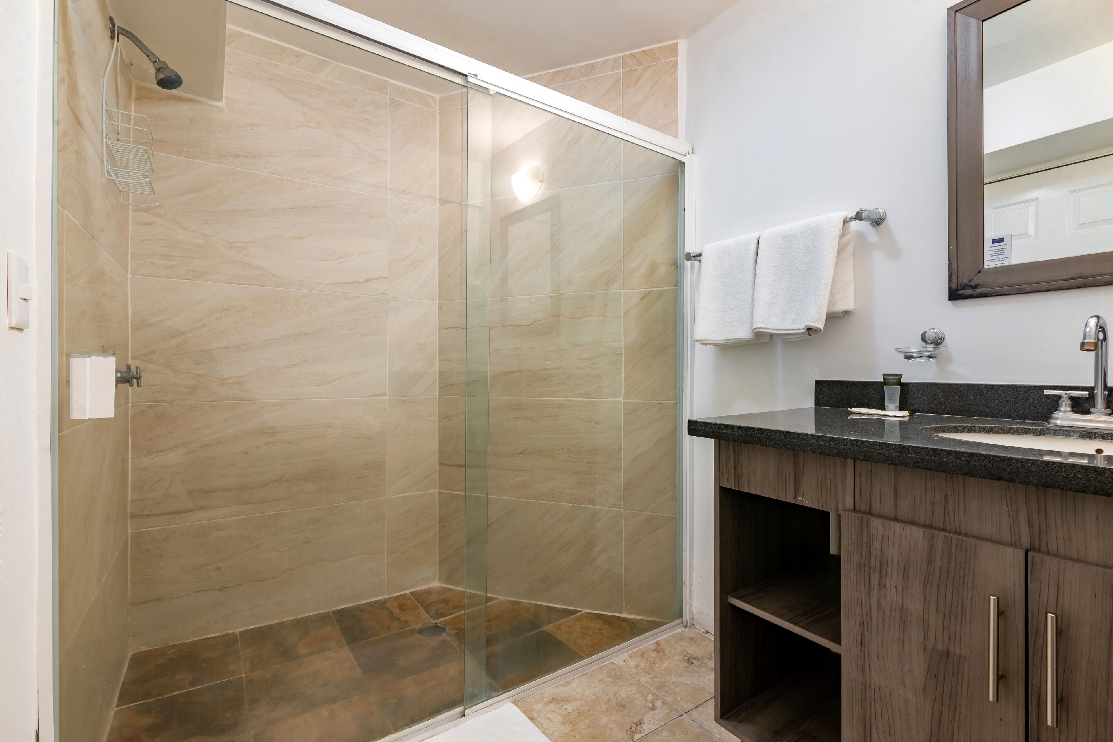 A modern bathroom with a glass-enclosed shower, a sink with a dark countertop, and wooden cabinets.