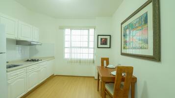 A kitchen with white cabinets, a dining table with chairs, a window with blinds, and a framed painting on the wall.