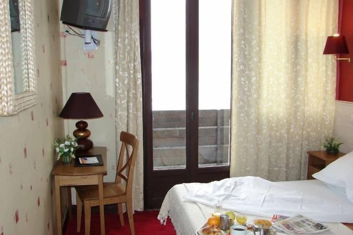 Hotellihuone, jossa on sänky, työpöytä, tuoli, televisio ja parveke.