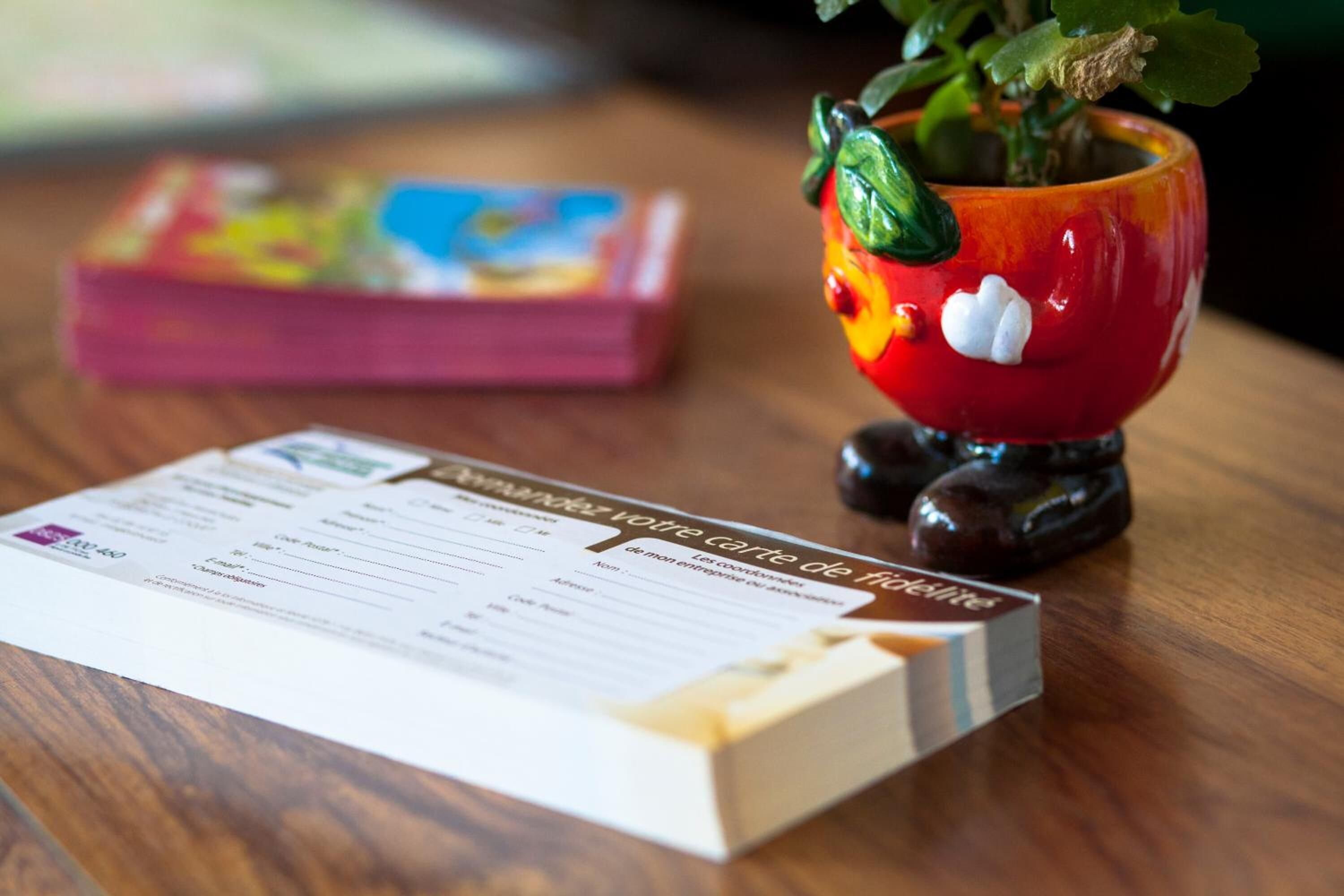 A wooden table with a menu, a colorful box, and a decorative red vase with a plant.