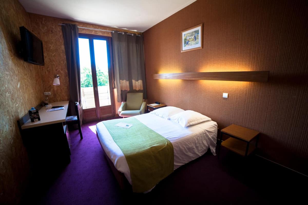 Hotellihuone, jossa on sänky, työpöytä, tuoli ja pieni pöytä.