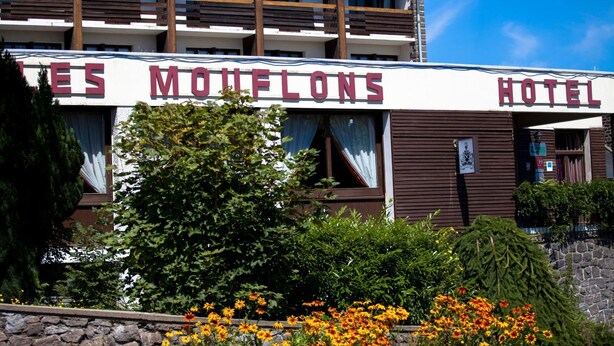 Un hotel llamado "LES MOULONS HOTEL" de estilo arquitectónico tradicional, con fachada de piedra y balcones de madera.