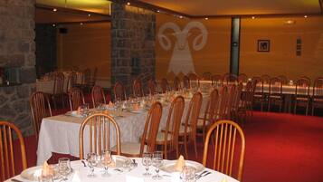 A banquet hall with round tables set for dining, wooden chairs, and a stone wall with a ram logo.