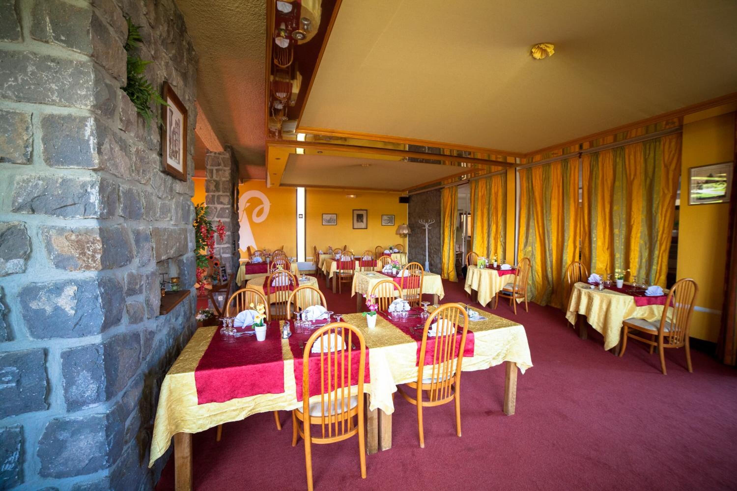 A dining area with tables set for service, stone walls, and a yellow carpeted floor.