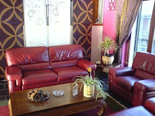 A red leather sofa, a wooden coffee table with decorative items, and a potted plant. - Le Grand Hôtel de Besse (Besse-et-Saint-Anastaise)