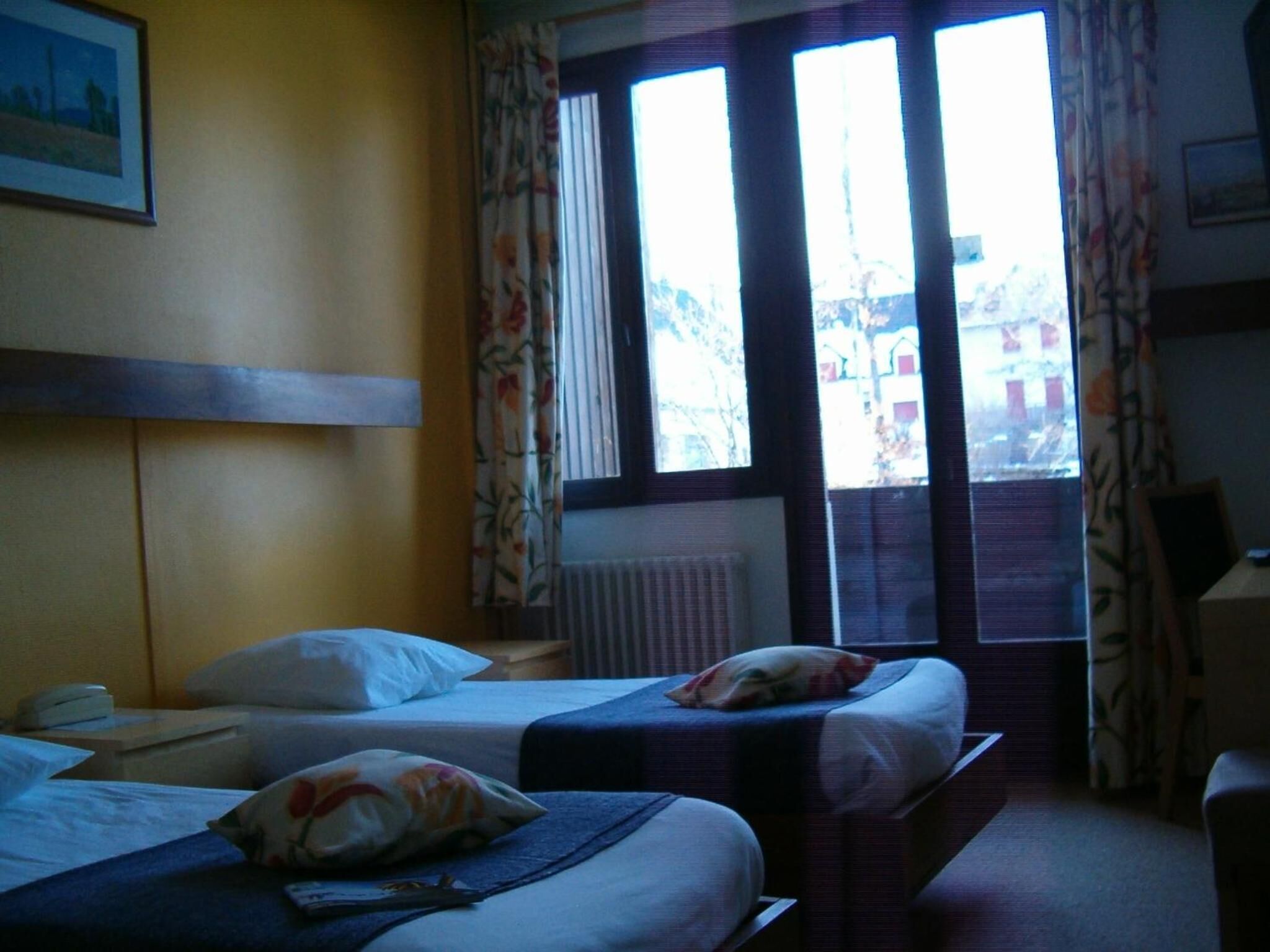 Une chambre d’hôtel avec deux lits, un radiateur, un bureau et une fenêtre avec des rideaux.