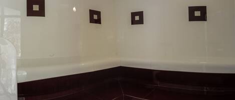 A corner of a bathroom with a dark-colored bathtub, white walls, and three square light fixtures.