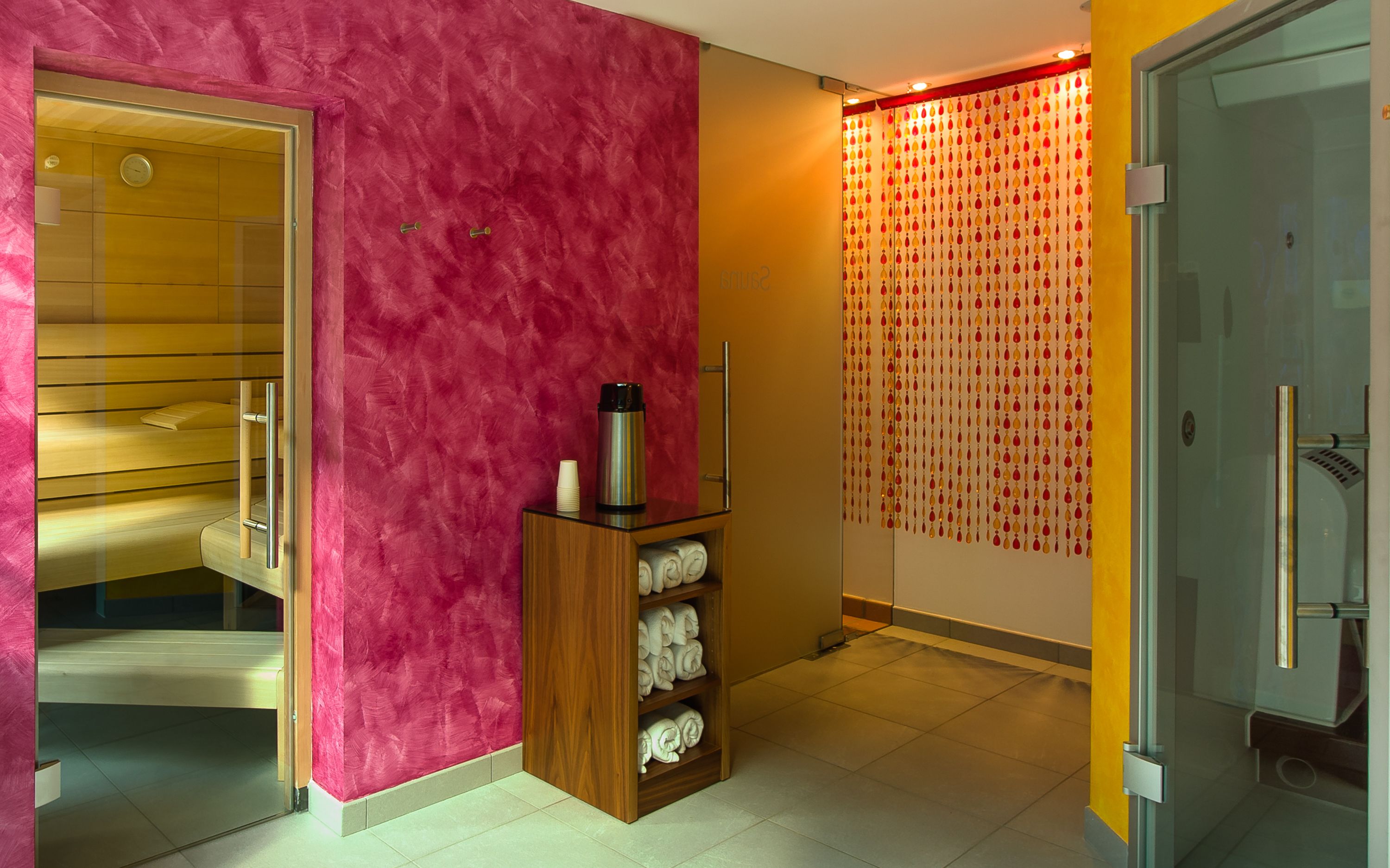 A modern hotel room with a sauna, a wooden shelf with towels, and a patterned curtain.