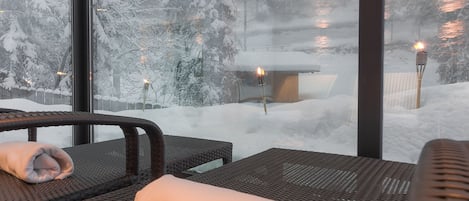 A cozy room with a view of a snowy landscape, featuring a window, a chair, and a table with a towel.