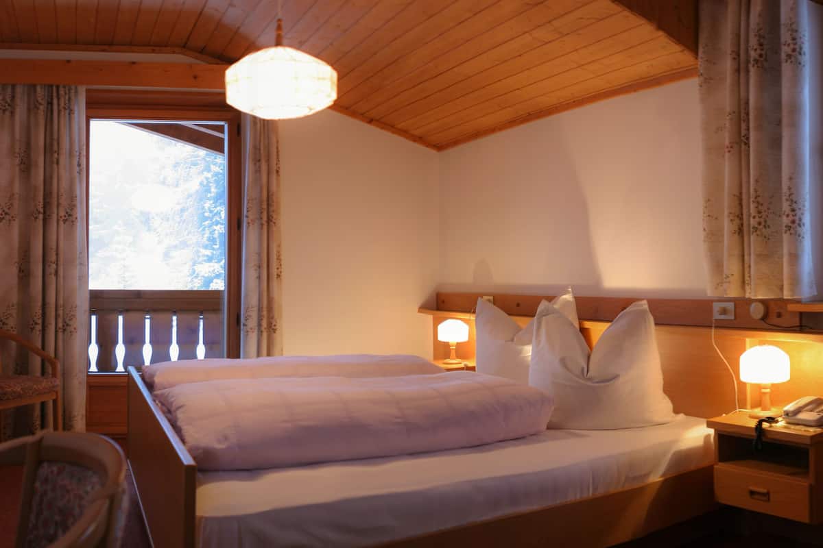 A bedroom with a wooden headboard, a bed with white linens, two bedside lamps, and a window with curtains.