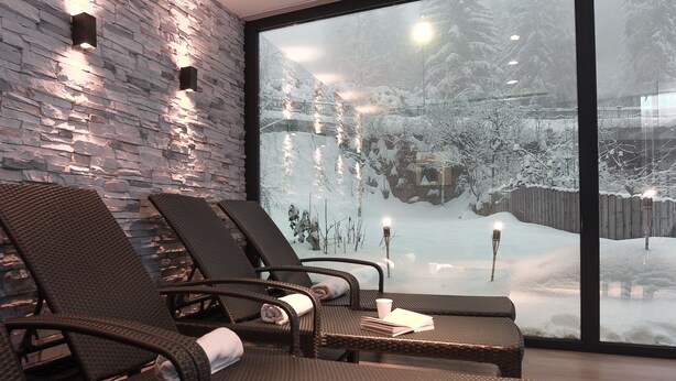 A spa area with wicker chairs and a stone wall, overlooking a snowy landscape. - Hotel Adler (Nova Levante)