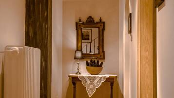 A hallway with a radiator, a table with a lace tablecloth, a lamp, and a mirror with a picture frame.