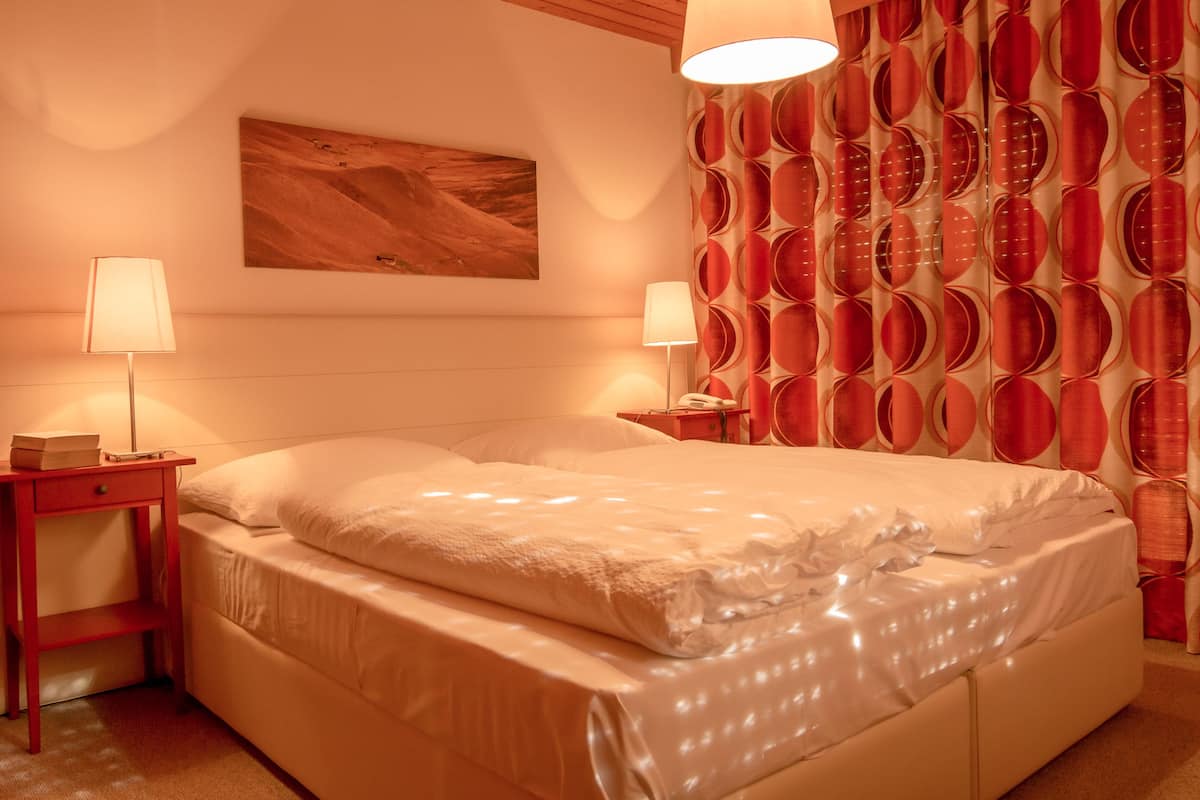 A hotel room with a large bed, two bedside tables with lamps, a wall-mounted painting, and a curtain with a circular pattern.