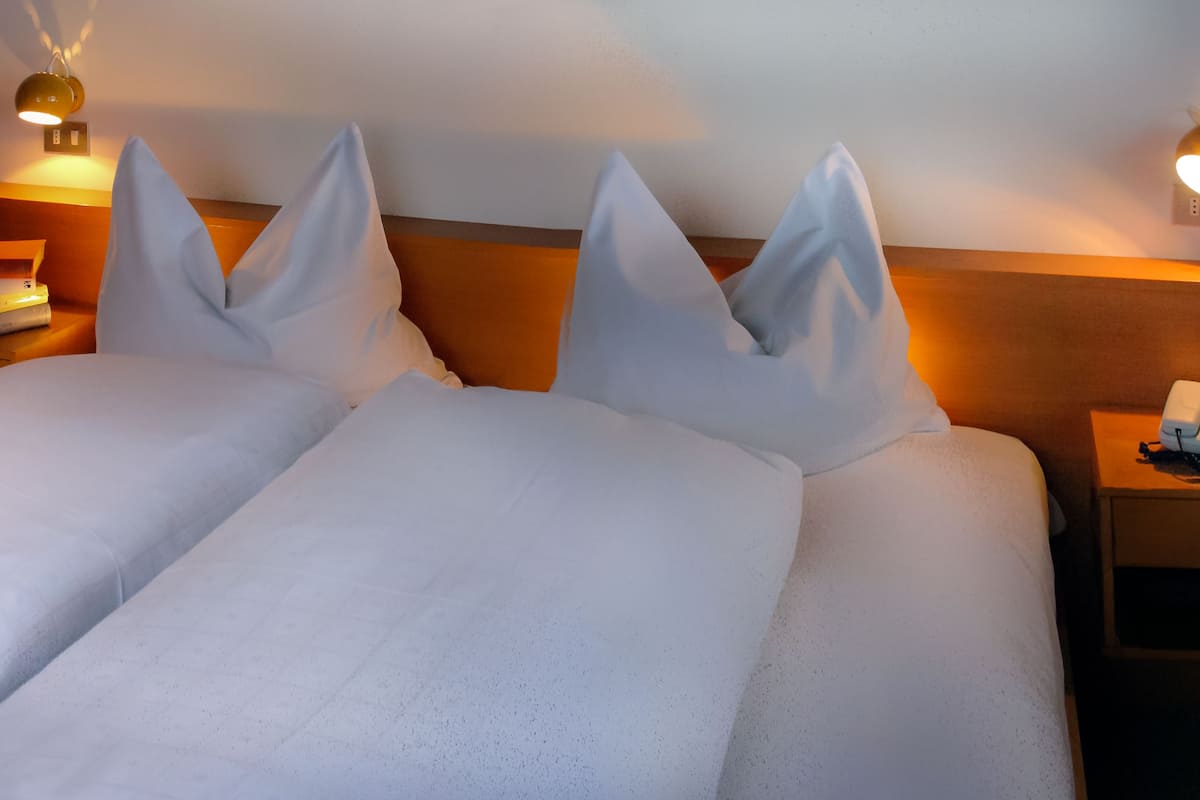 A hotel room with two beds, each with white linens and pillows, a wooden headboard, bedside tables with lamps, and a telephone.