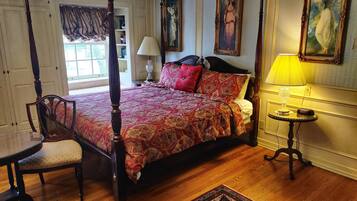 A four-poster bed with a patterned bedspread, a chair, a bedside table with a lamp, and a rug on a wooden floor.