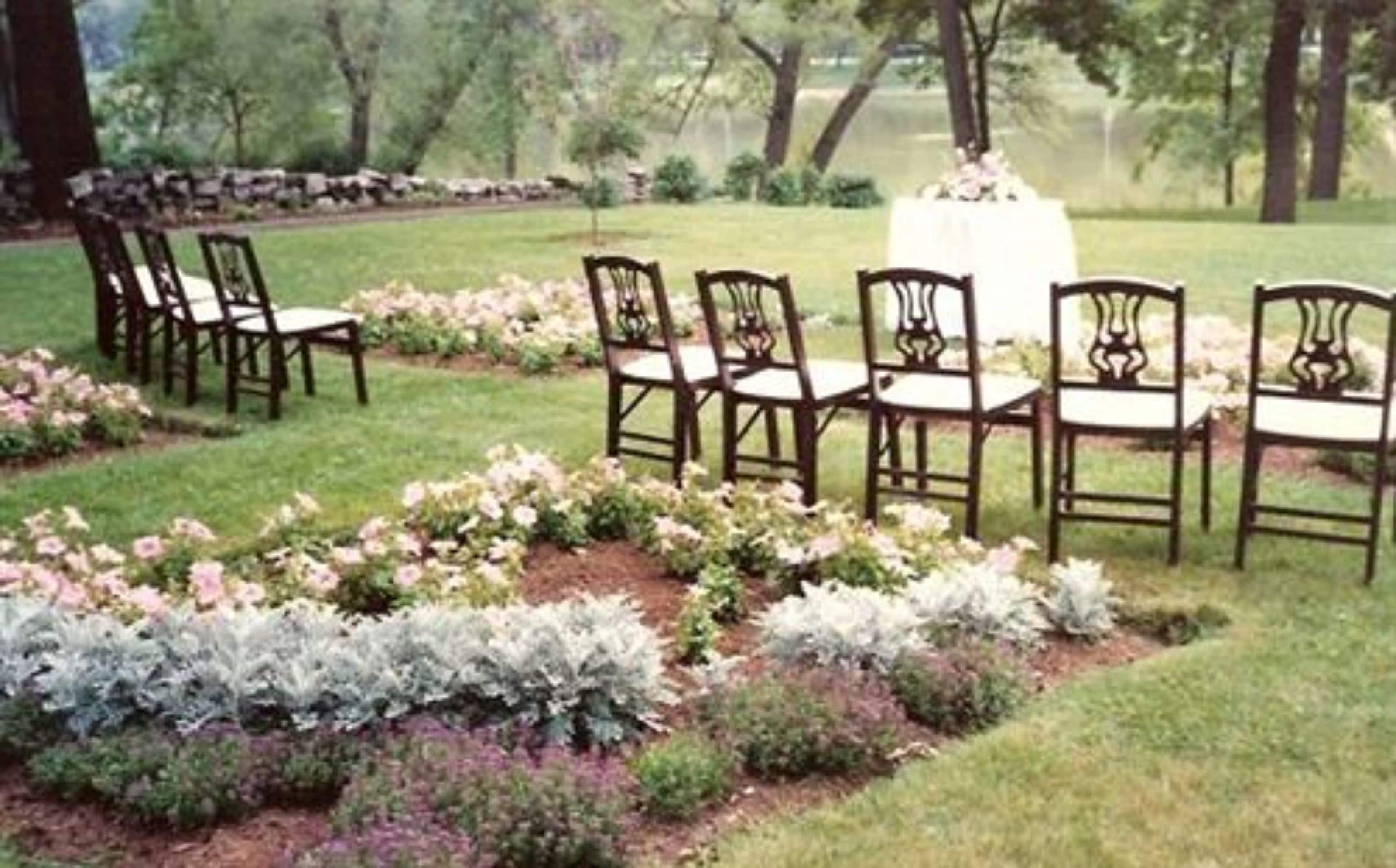 A garden setting with a table and chairs arranged for an outdoor event.