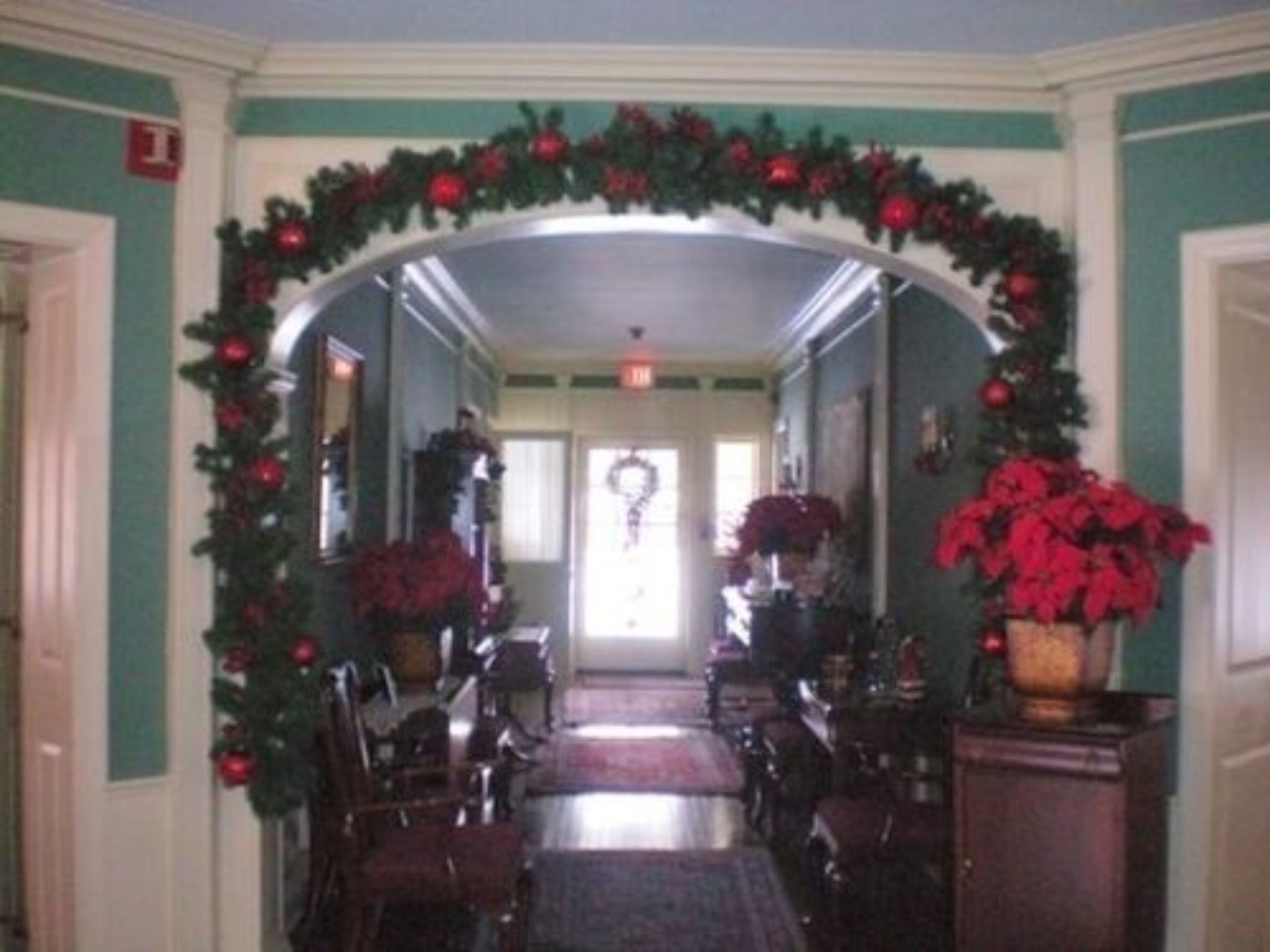 A hallway with a Christmas arch decorated with red ornaments and greenery, leading to a door with a wreath.